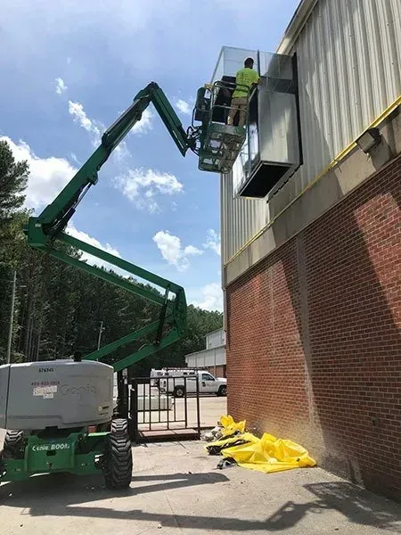 Man on lift installing metal unit on exterior wall. Blue sky.