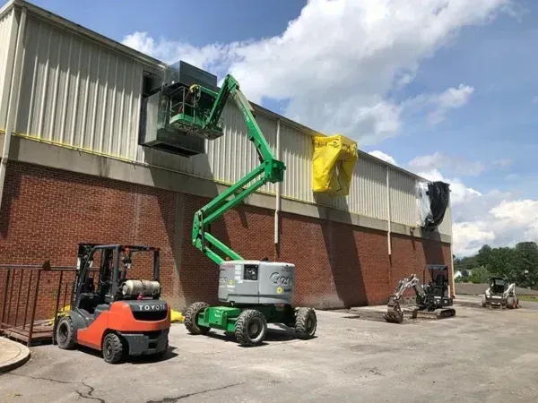 Construction site with a boom lift, forklift, and excavators working on a building with a brick base and metal siding.