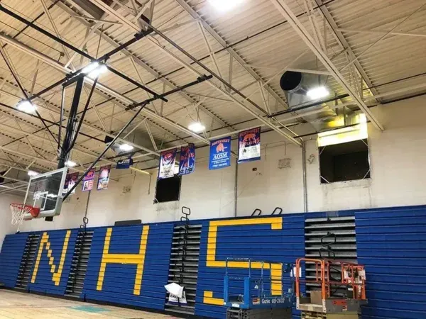 Gymnasium interior with blue and yellow walls, basketball hoop, banners, and lights.