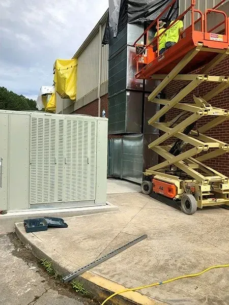 A worker in a lift paints exterior building vents, near an equipment box.