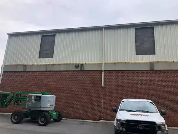 Brick building with white metal siding, boarded-up windows, a cherry picker, and a white truck.