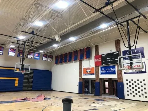 Basketball court interior with hoops, banners, scoreboard, and blue and white walls.