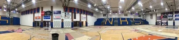 Interior of a gymnasium. Wood floor. Blue and white walls. Banners hang from the ceiling. Basketball court in the foreground.