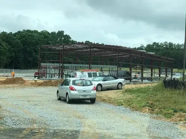 Cars parked near a steel frame building under construction on a cloudy day.