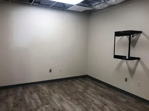 Empty room with gray walls, wood-look floor, and a black wall-mounted shelf.