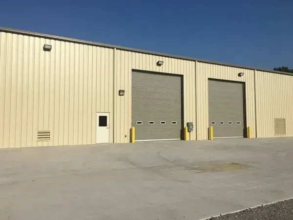 Beige industrial building with two large garage doors and a small white door.