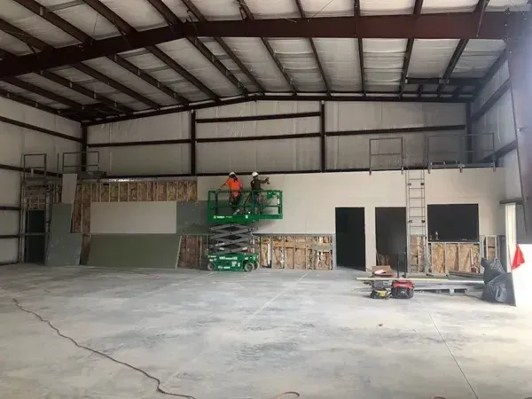 Interior view of a warehouse under construction. Two workers on a lift, building a wall.