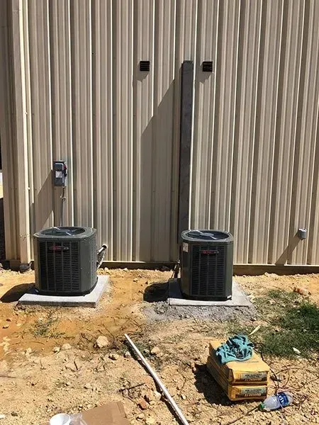 Two AC units on concrete pads outside a building, electrical components visible.