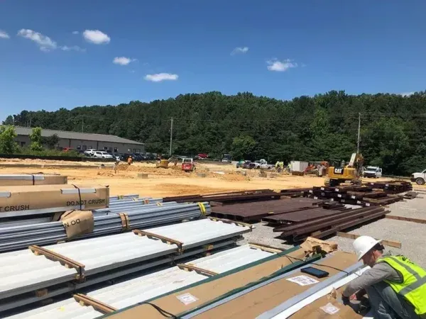 Construction site with equipment, materials, and a worker in a high-visibility vest.