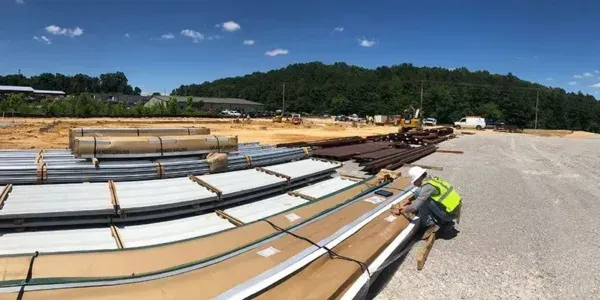 Construction worker in safety vest inspects panels on a sunny construction site, with dirt and mountain in the background.