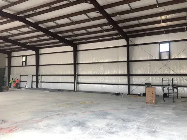 Interior of a large steel-framed building under construction with concrete floor, walls, and ceiling.