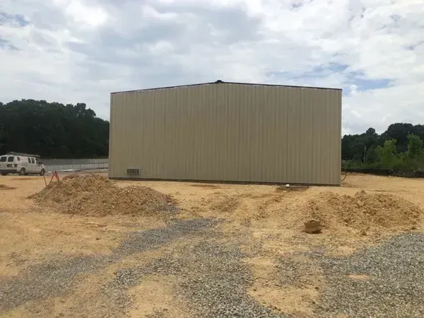 Tan metal building on a dirt lot, piles of wood chips, overcast sky.
