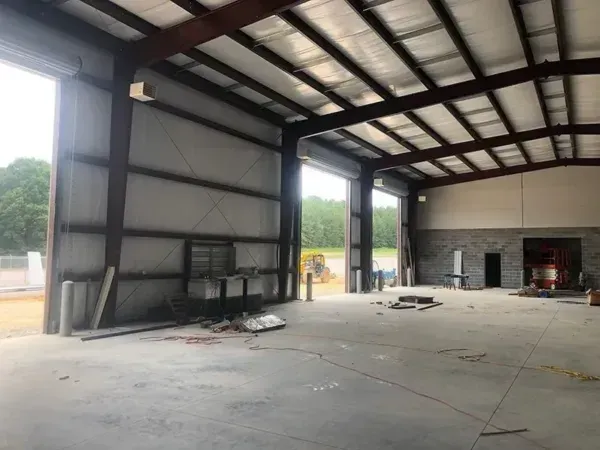 Empty steel-frame building interior with large open doors, concrete floor, and exposed ceiling beams.
