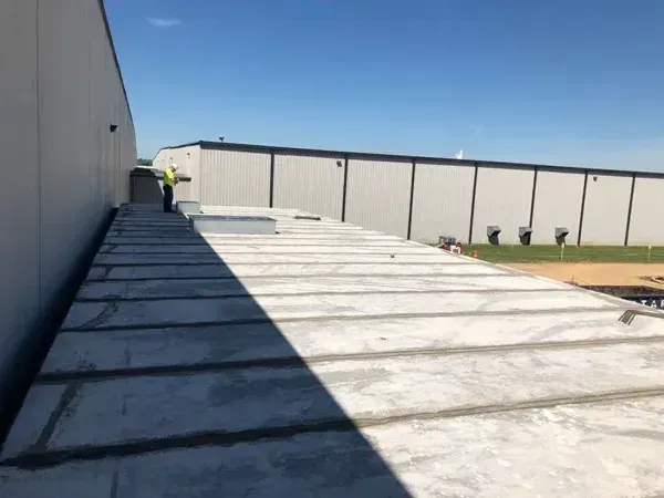 Construction worker on a concrete roof with an industrial building in the background on a sunny day.