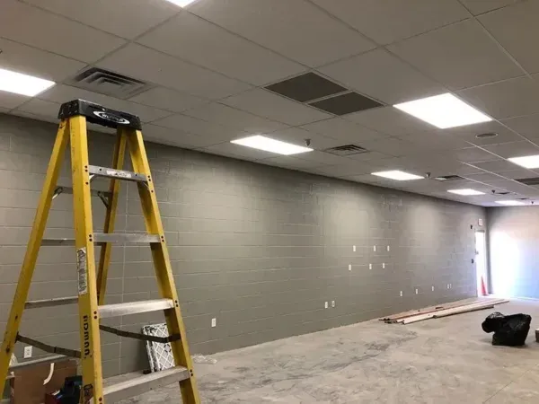 Yellow ladder against a gray cinder block wall. Room under construction with ceiling lights.