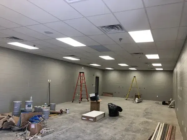 Interior construction site; empty room with gray walls, drop ceiling, tools and materials scattered on the floor.