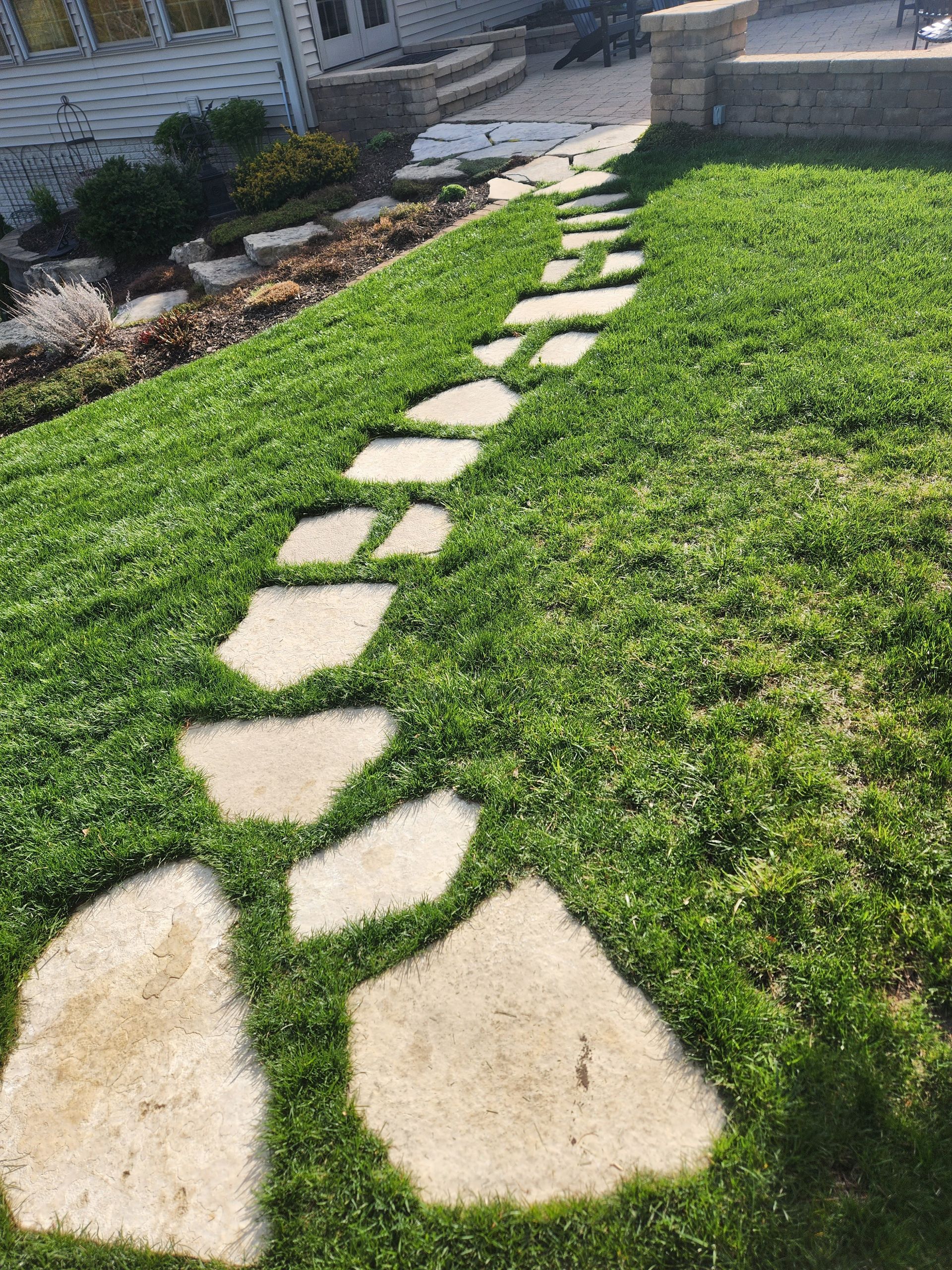 Stone pathway through a grassy yard, leading uphill towards a house.