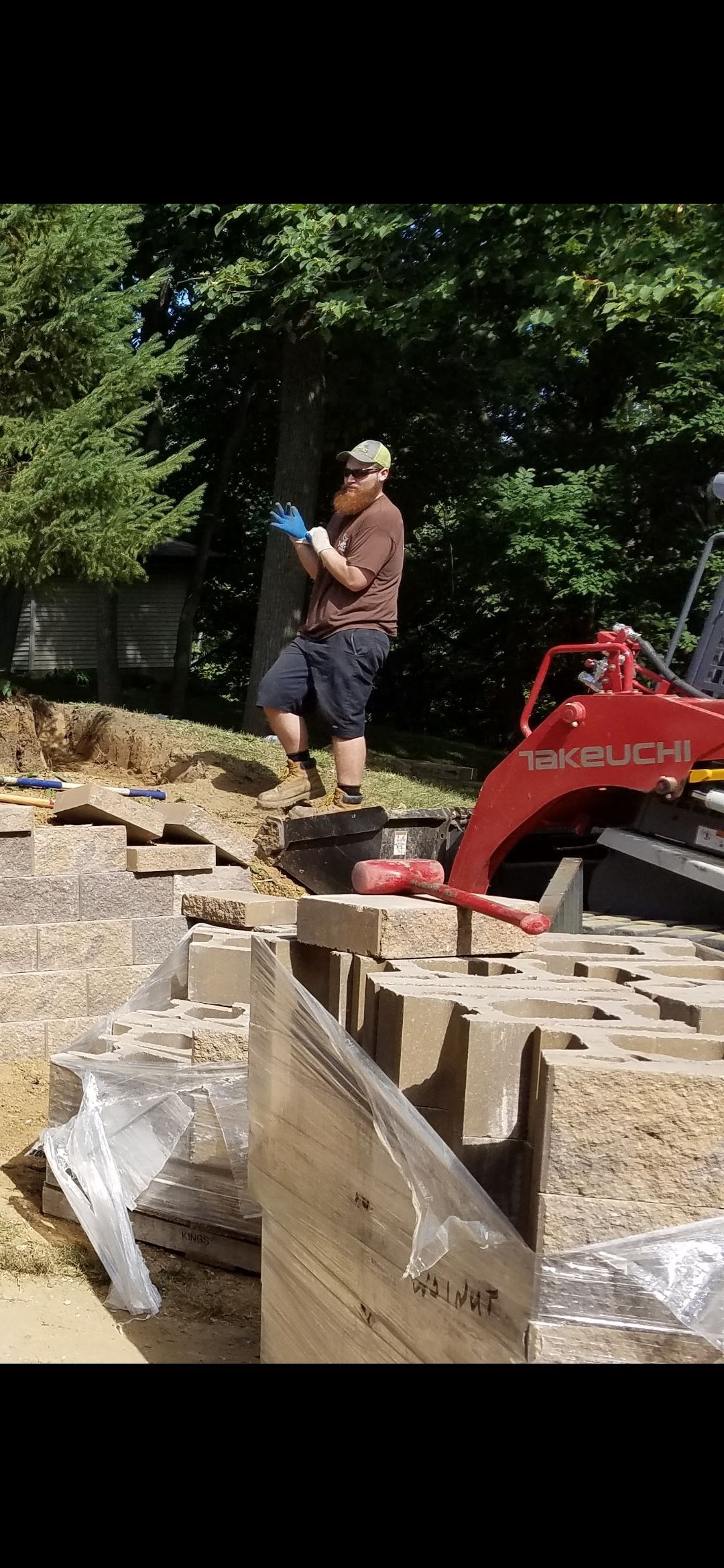 A person in work clothes near a small digger on a construction site with building materials.