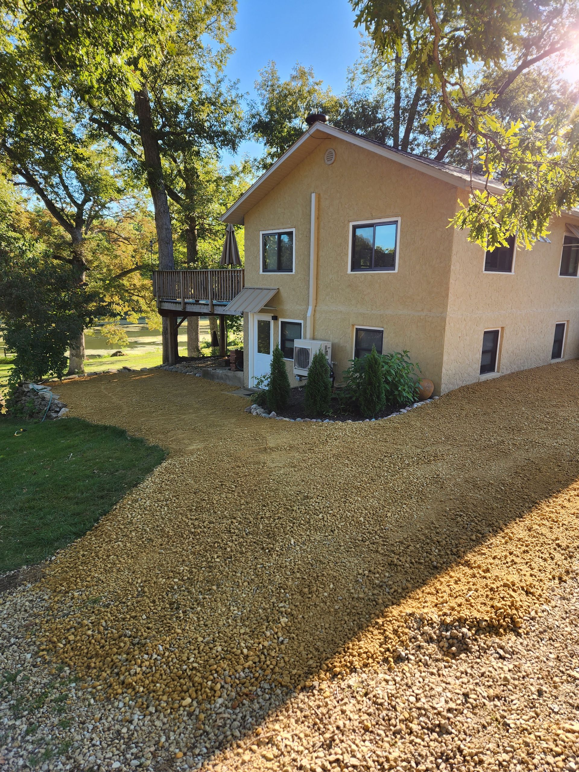 House with gravel driveway and treehouse, surrounded by trees and green grass on a sunny day.