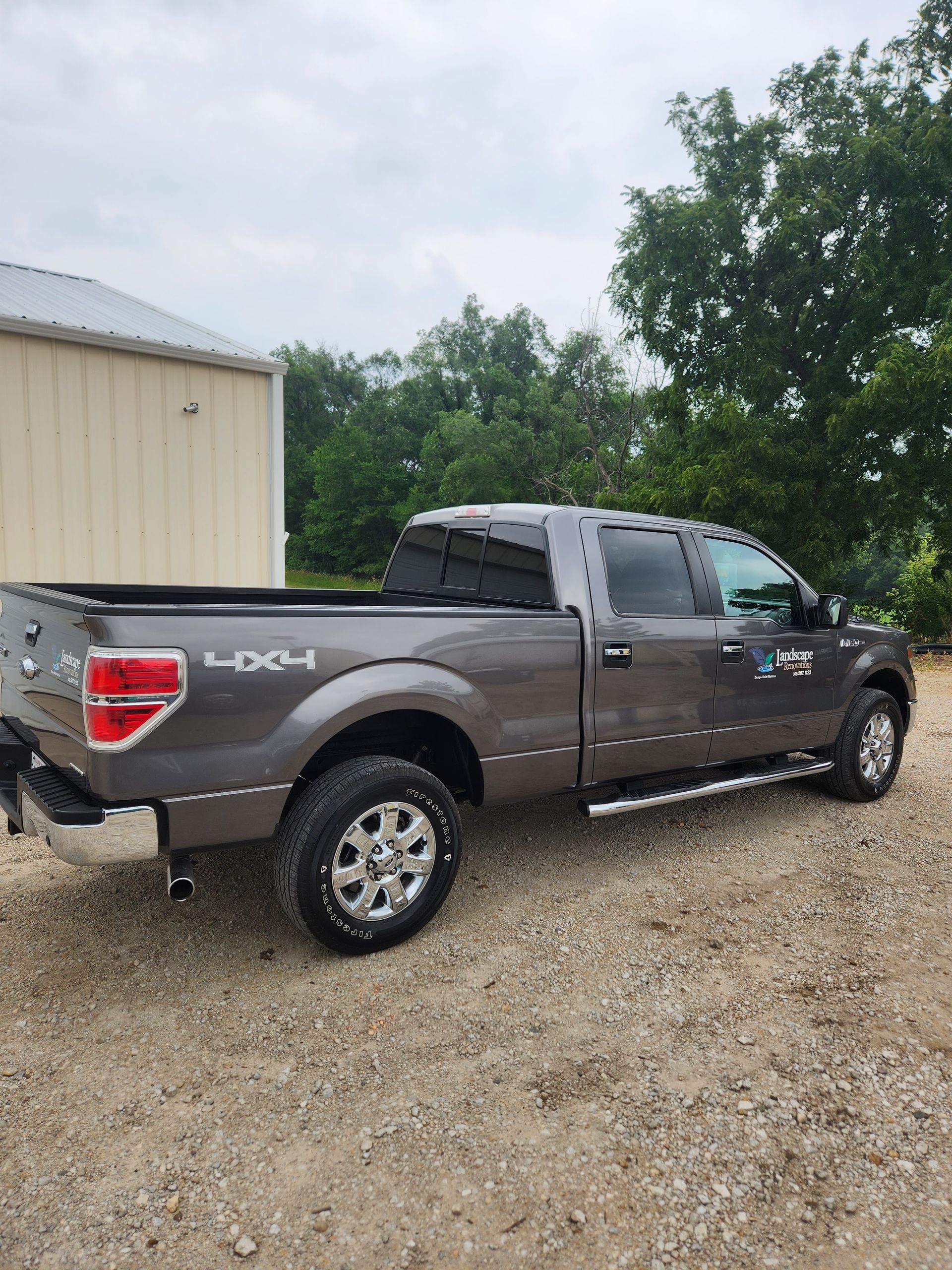 Gray Ford F-150 truck parked on gravel in front of a white building with trees in the background.