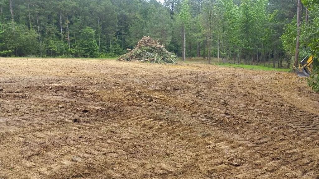 Plowed field with a pile of brush in the background, surrounded by trees.