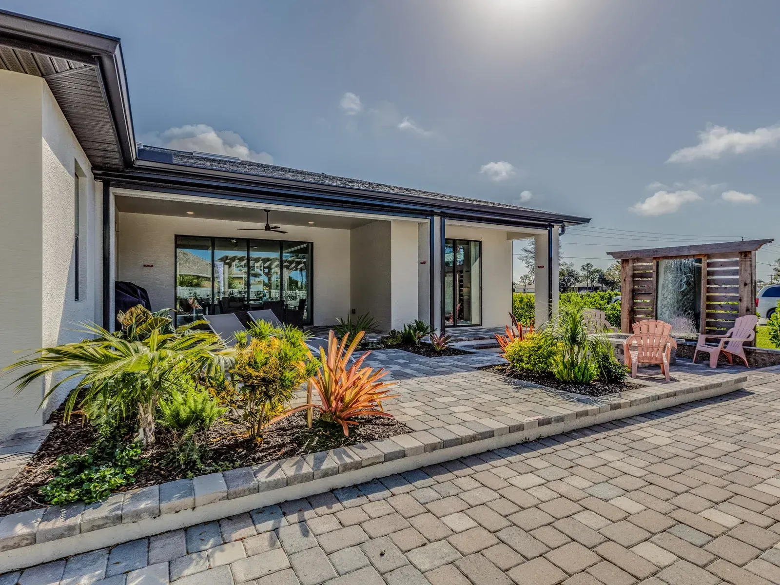 Back patio of a house with paved stones, plants, and seating under a pergola.