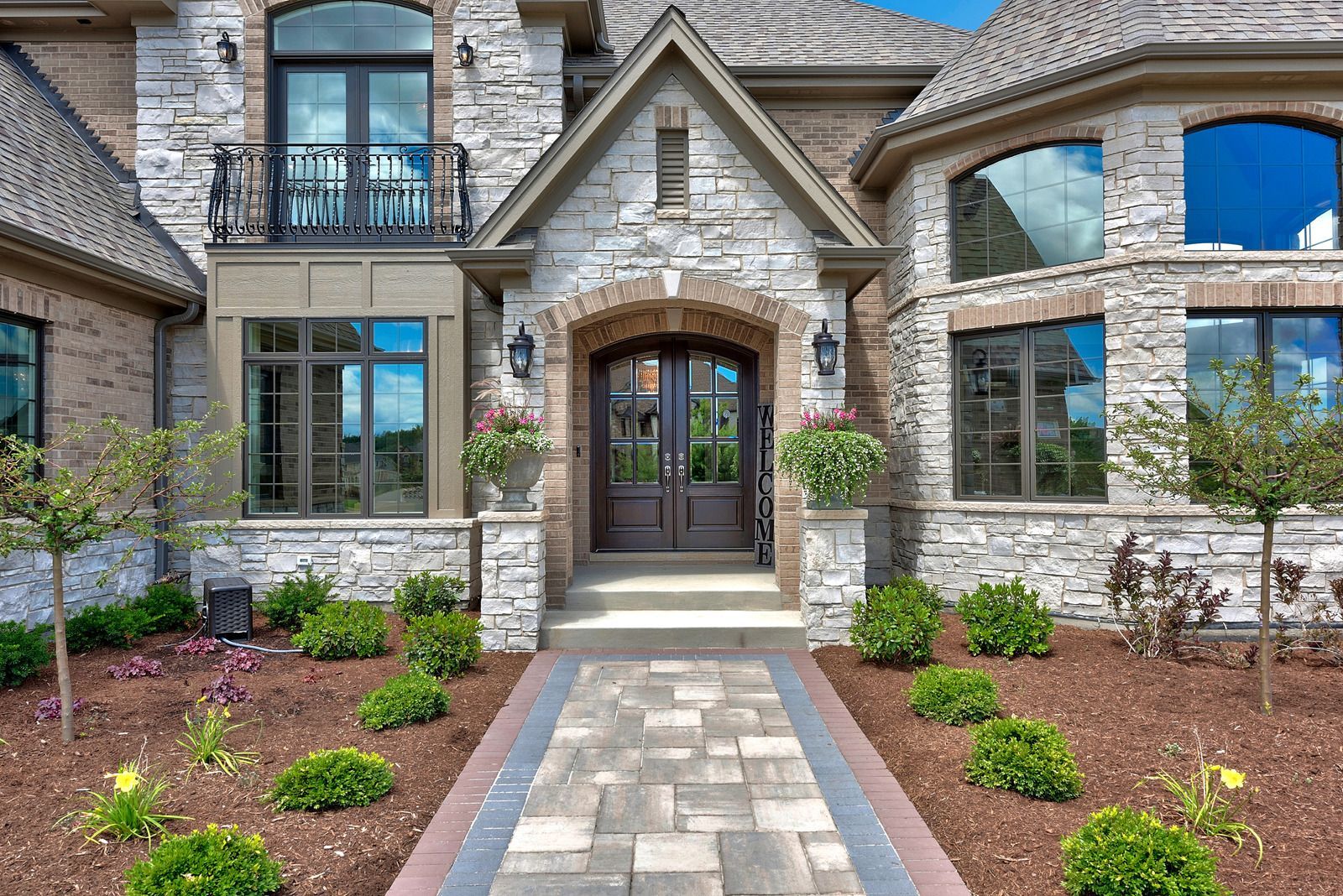 Stone facade house with dark double doors, arched entryway, and landscaped front yard.