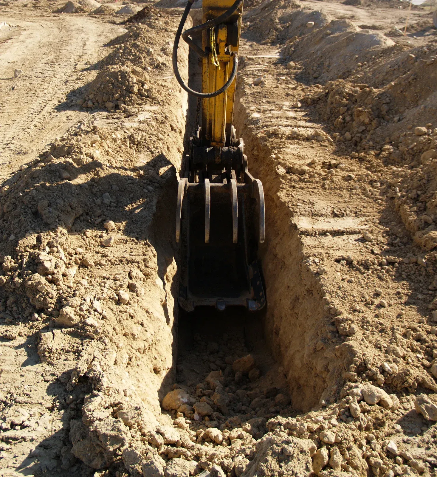 Yellow excavator digging a trench in sandy soil at a construction site.
