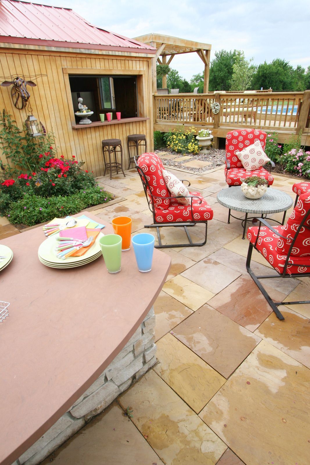 Outdoor patio with seating, bar, and flower beds. Bright colors, brick patio, red accents.