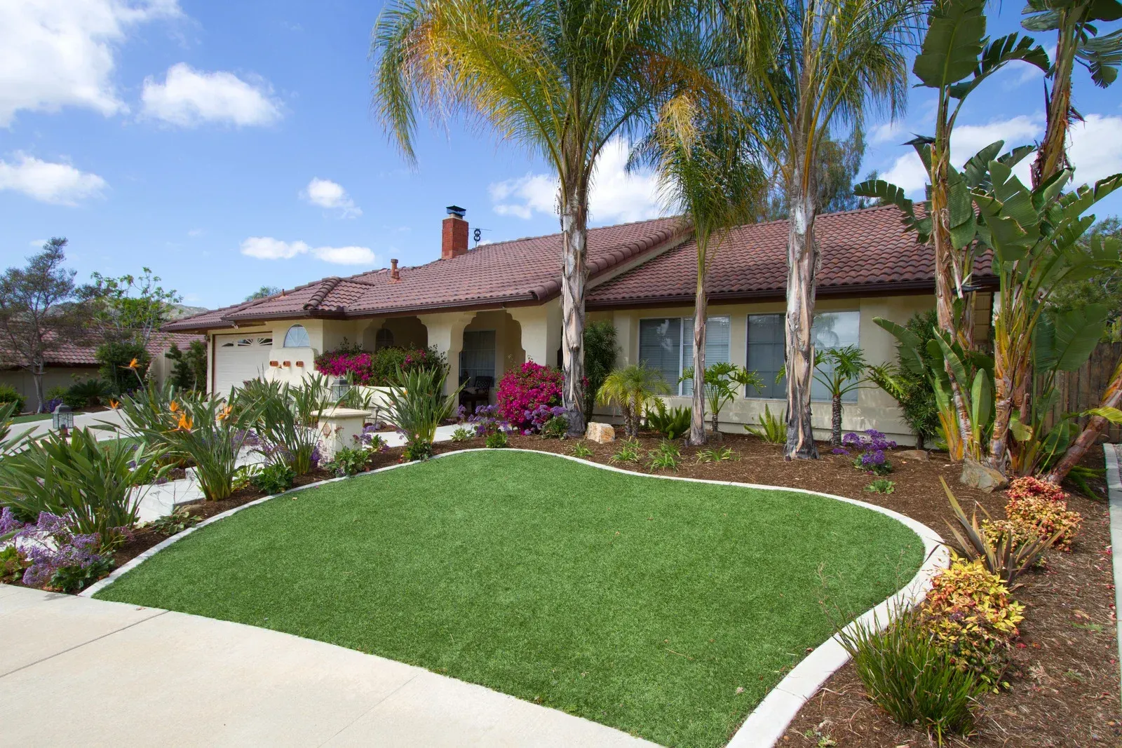 A ranch-style house with manicured lawn, landscaping, and palm trees under a blue sky.