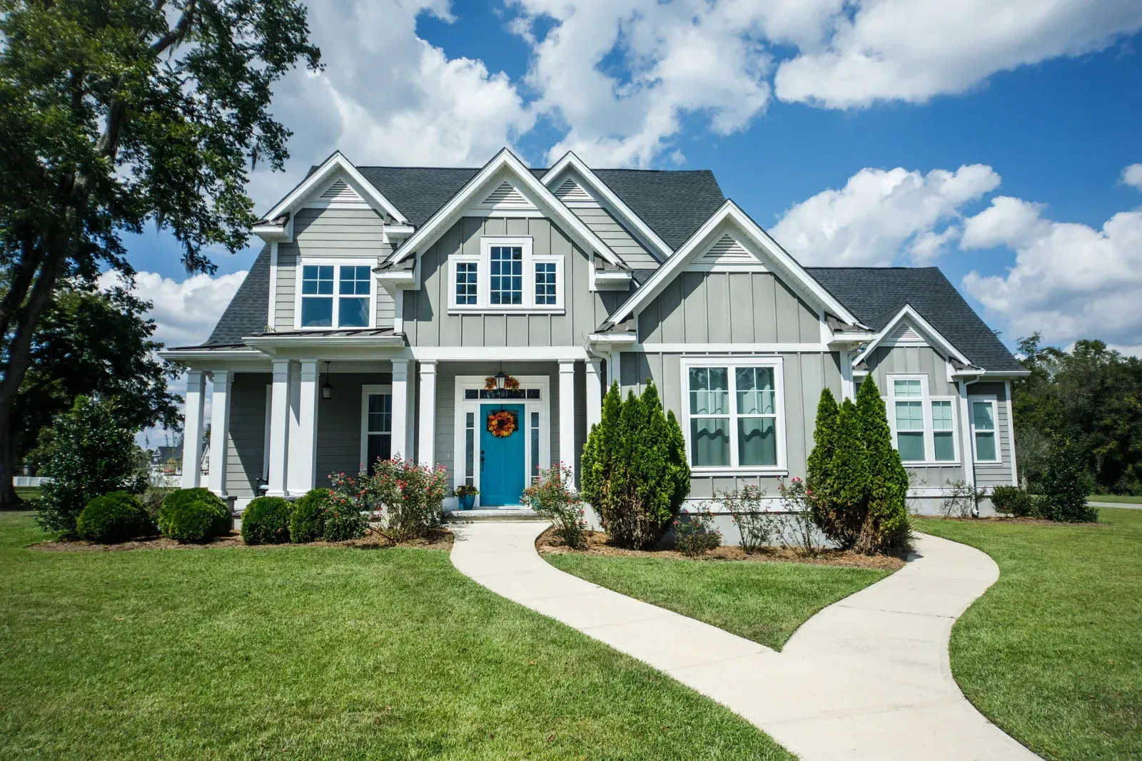 Gray house with blue door, white trim, green lawn, two curved walkways, blue sky.