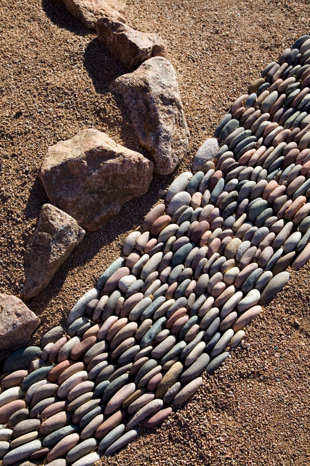 A rock pathway made of small, rounded stones curves through a gravel bed, with larger rocks bordering it.