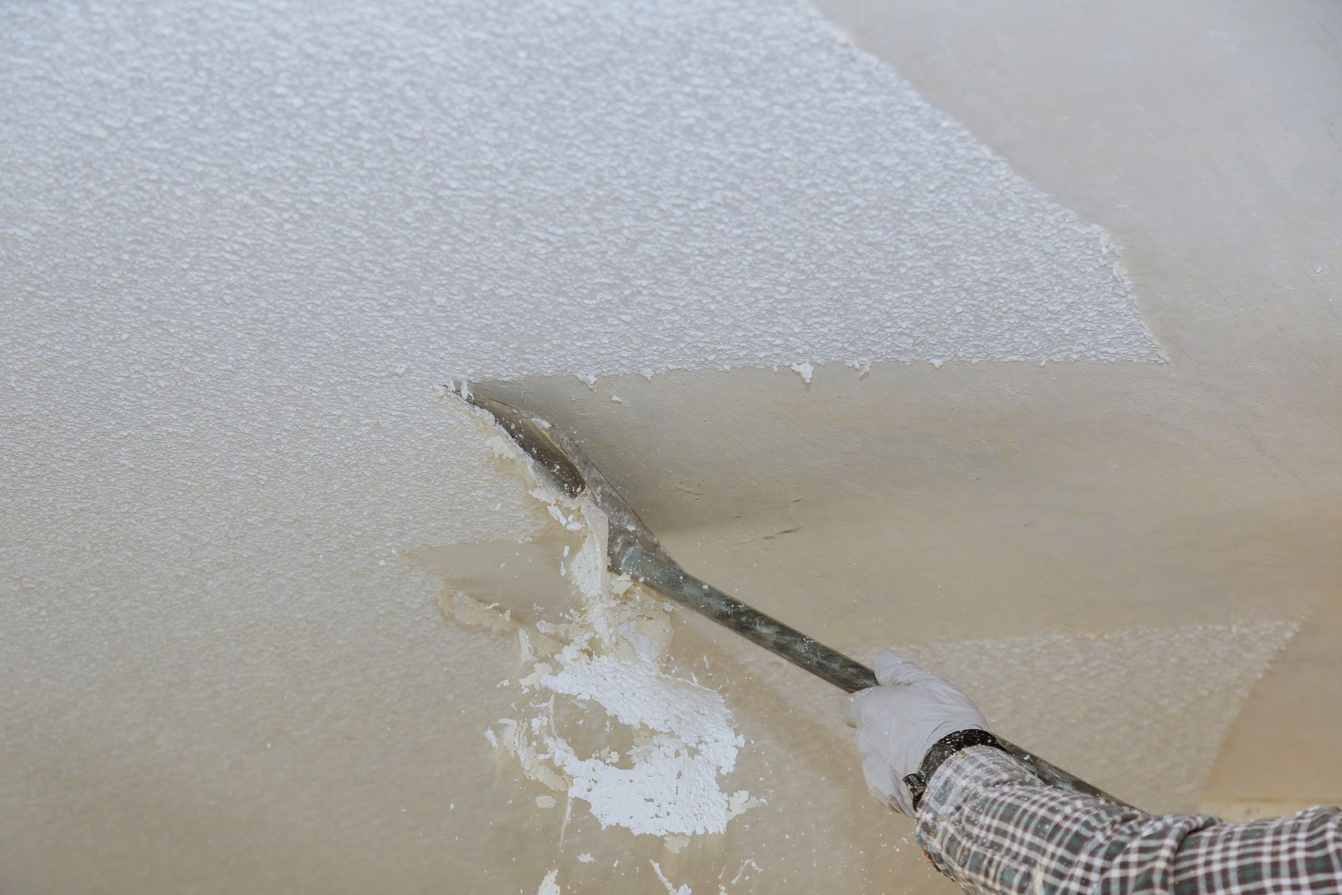 Person scraping textured ceiling with a metal tool, removing a white coating.