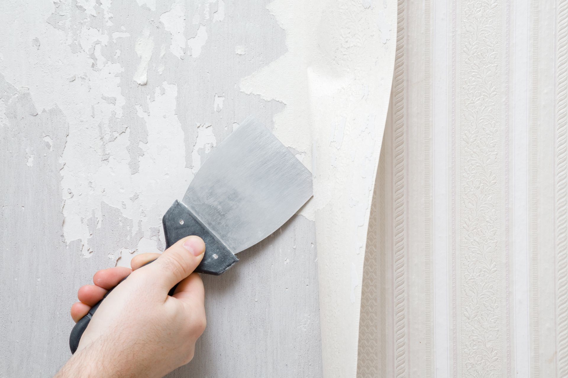 Person using a scraper to remove striped wallpaper from a wall.