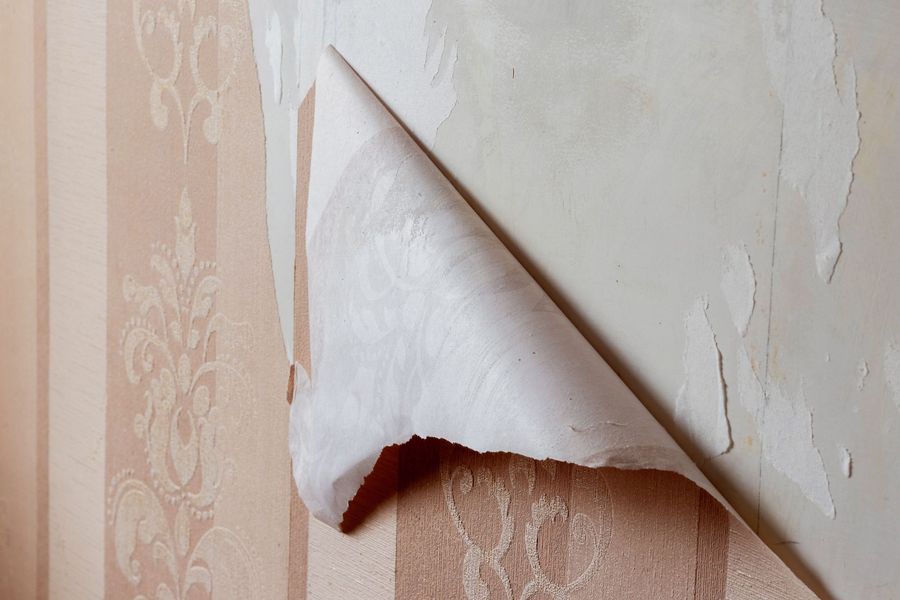 Wallpaper peeling off a wall, revealing a textured surface.