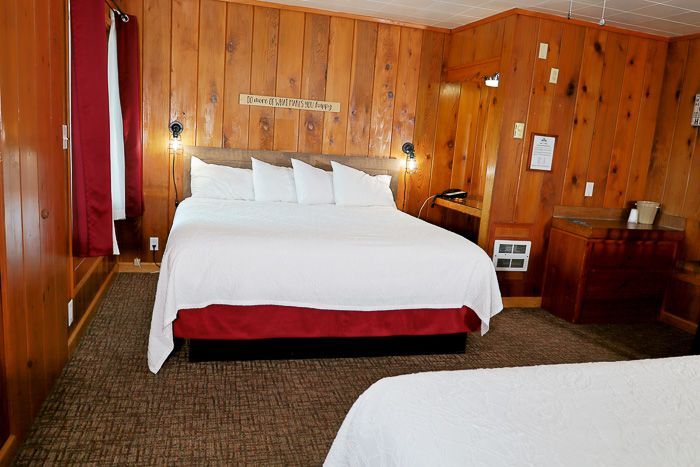Cozy wood-paneled hotel room with a large bed, red accents, and a dresser