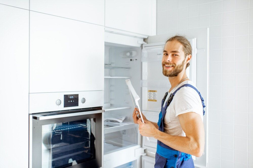 A Man is Working on a Refrigerator in a Kitchen — Todd Hayes Refrigeration & Air Conditioning Pty Ltd in Maclean, NSW
