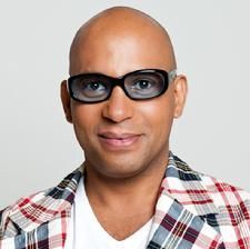 A bald man wearing glasses and a plaid jacket is smiling.