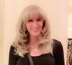 A woman with blonde hair is wearing a black shirt and smiling.