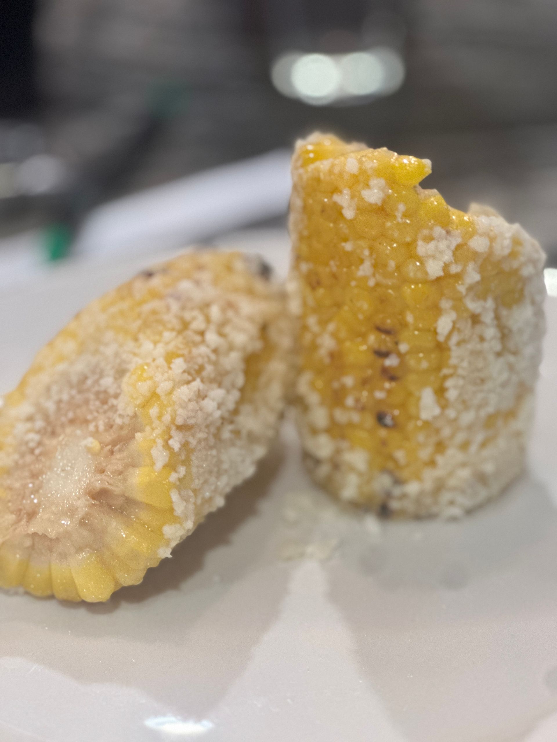 Two corn on the cob on a white plate with a bite taken out of one of them.