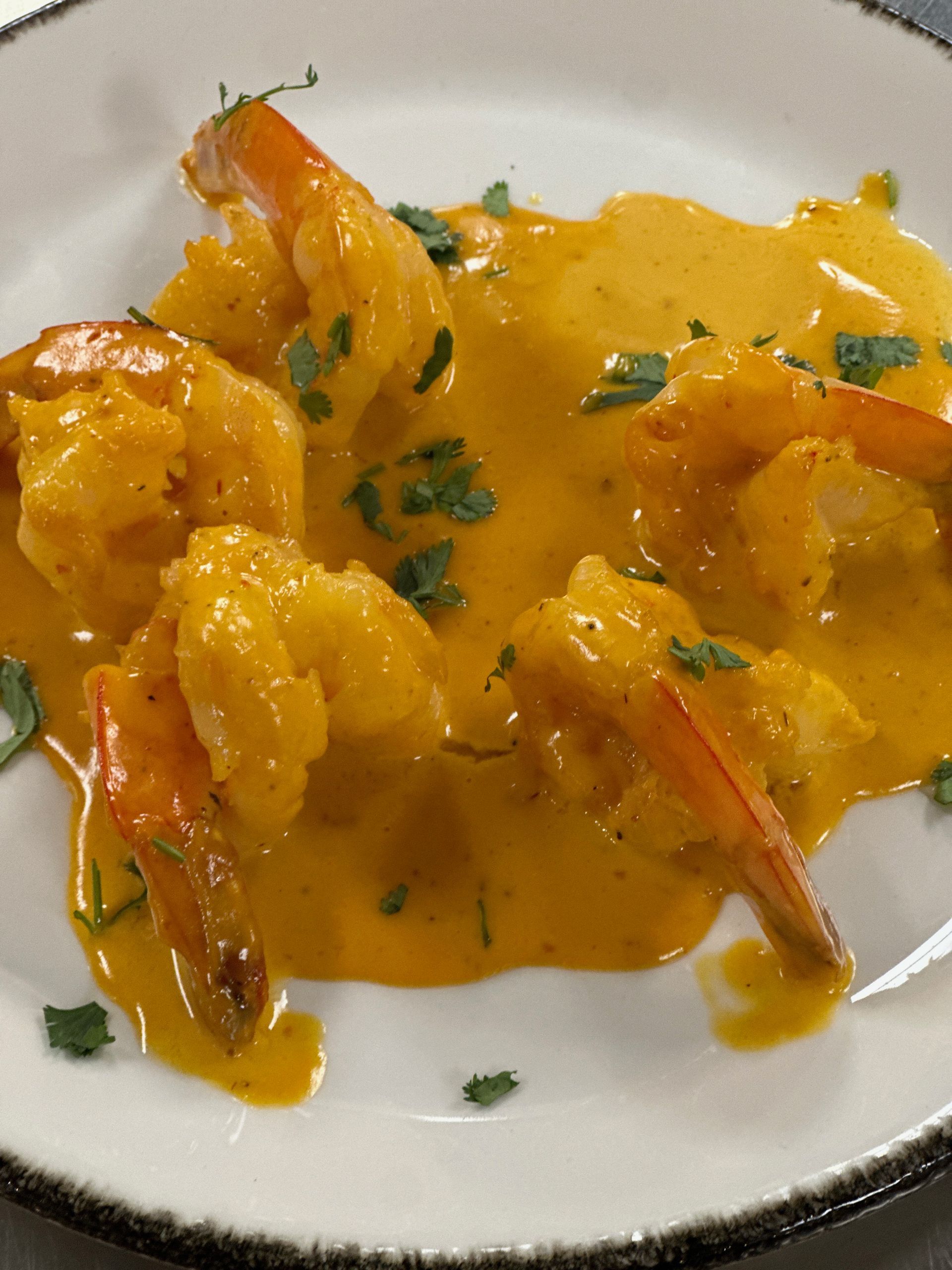 A white plate topped with shrimp and sauce on a table.