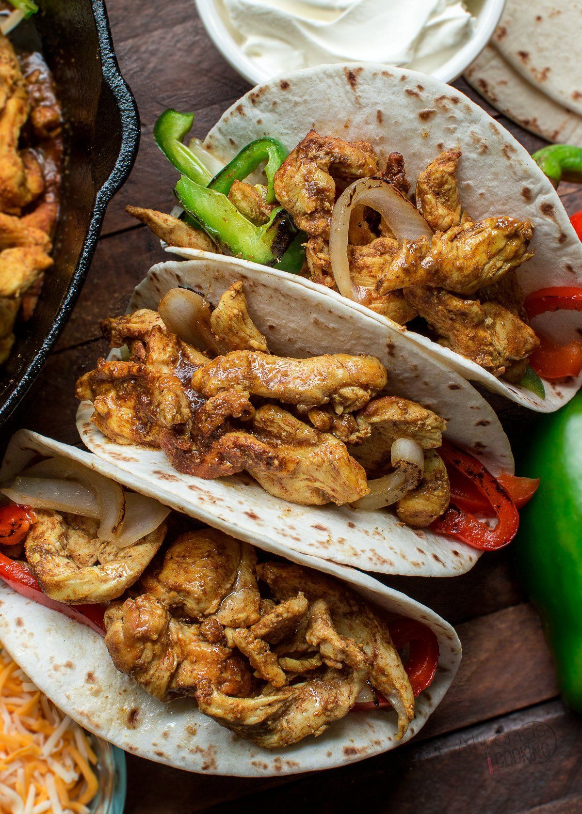 A close up of three chicken tacos on a wooden table.