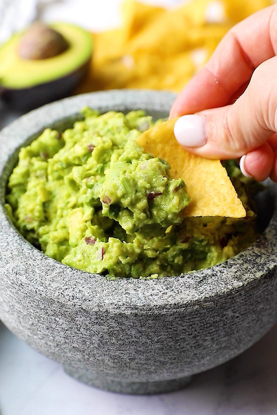 A person is dipping a tortilla chip into a bowl of guacamole.