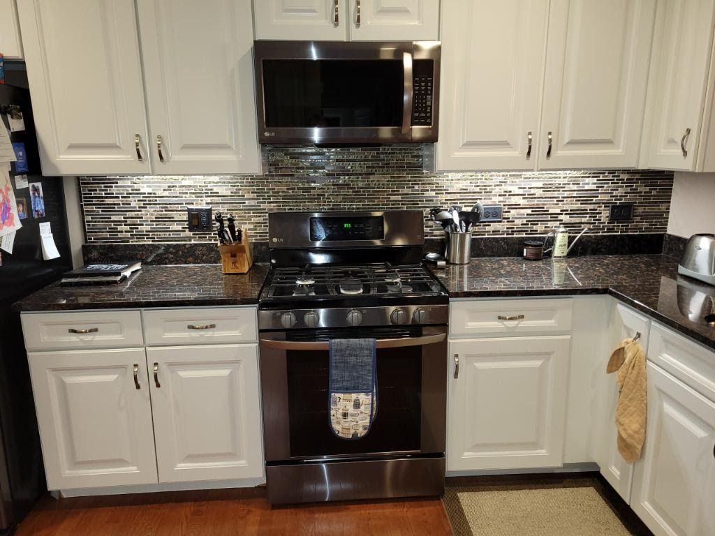 Modern kitchen with white cabinets, black appliances, and a stainless steel stove and microwave.
