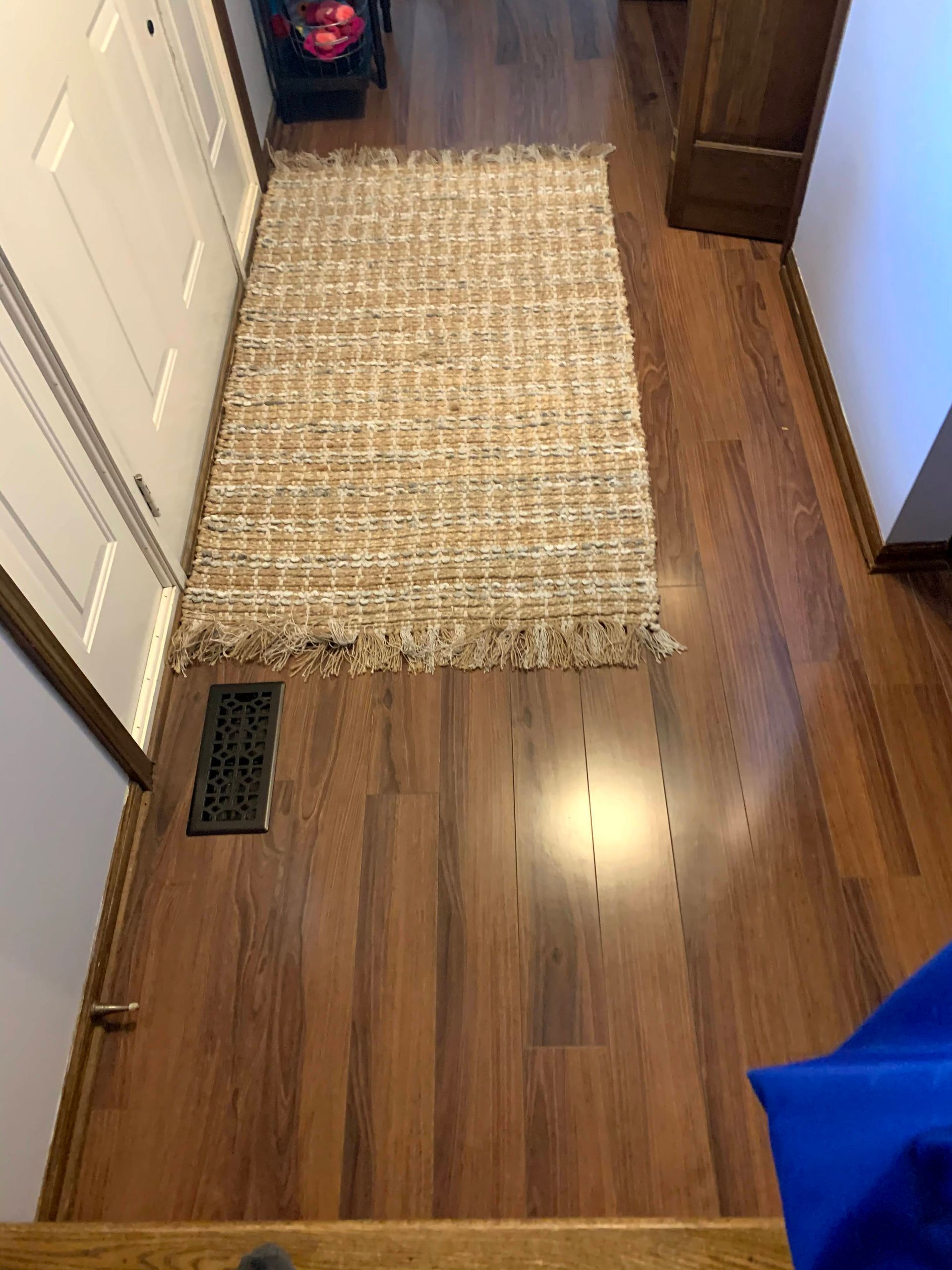 Narrow hallway with hardwood floor, beige rug runner, and a floor vent near a closet door.