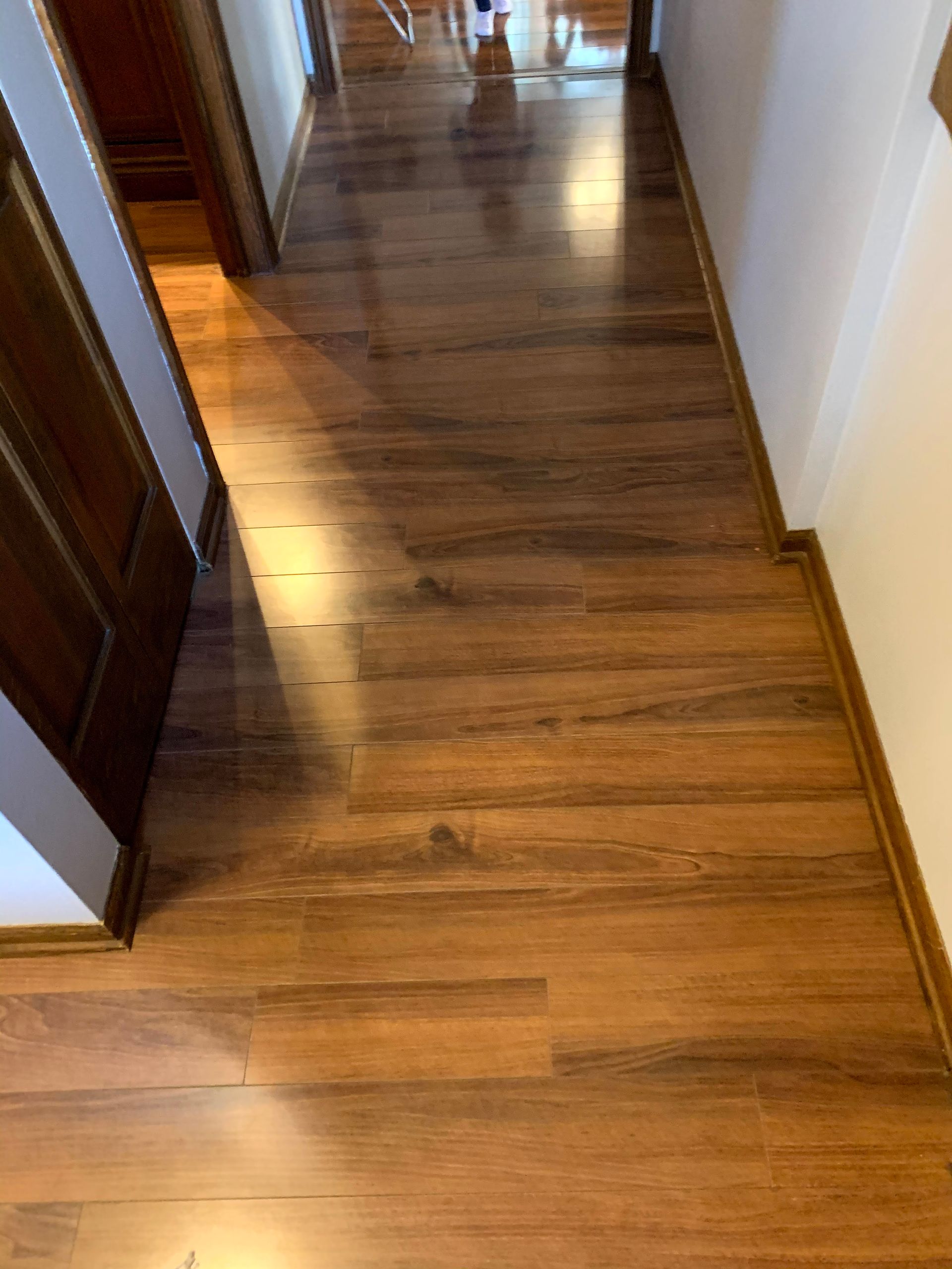 Narrow wooden hallway with polished floors, white walls, and doorways on both sides.