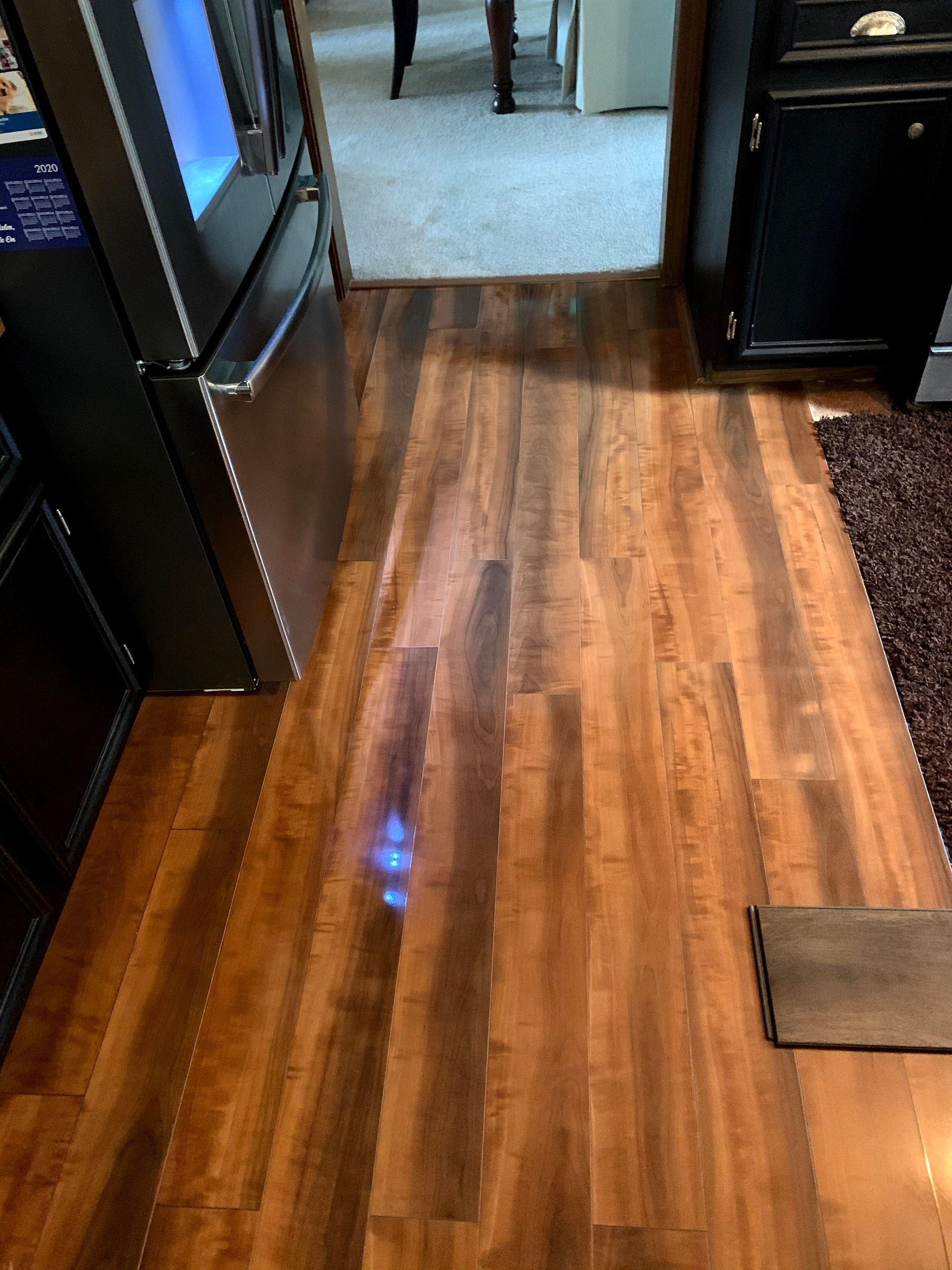 Wooden hallway floor with dark furniture and a carpeted room visible ahead