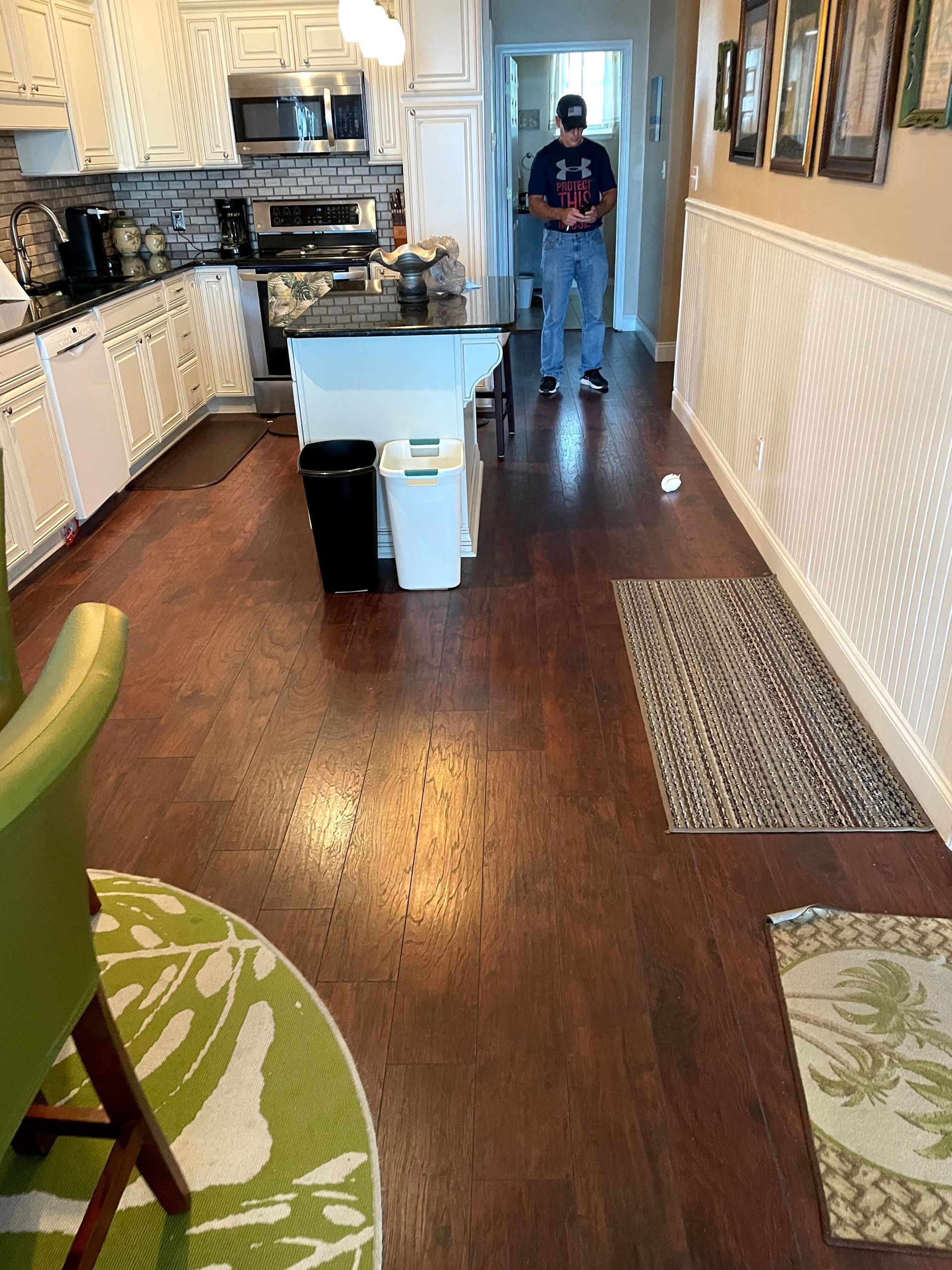 Narrow kitchen with dark wood floors, white cabinets, island, and a person standing at the far end.