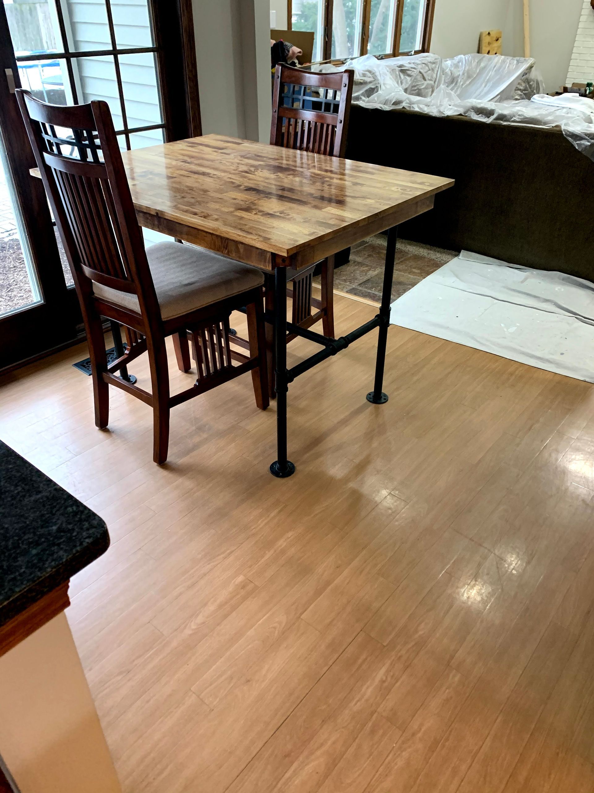 Wooden dining table with chairs in a bright room with hardwood floors and a window seat.