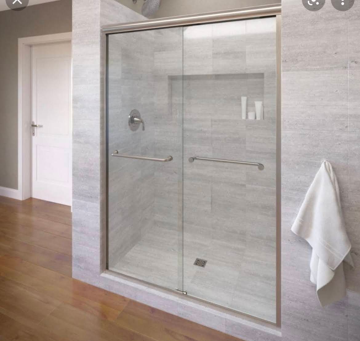 Modern bathroom with a glass shower enclosure, gray tile, wood floor, and white towel on the wall